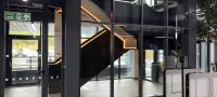 Modernes Gebäude-Interieur mit Glaswänden, schwarzer Treppe mit LED-Beleuchtung und einem Eingang mit Drehkreuz